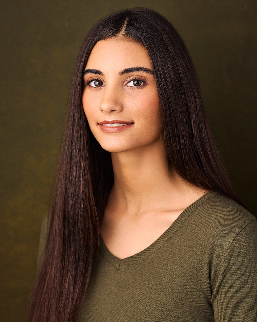 In this headshot, a young woman is wearing a green sweater.