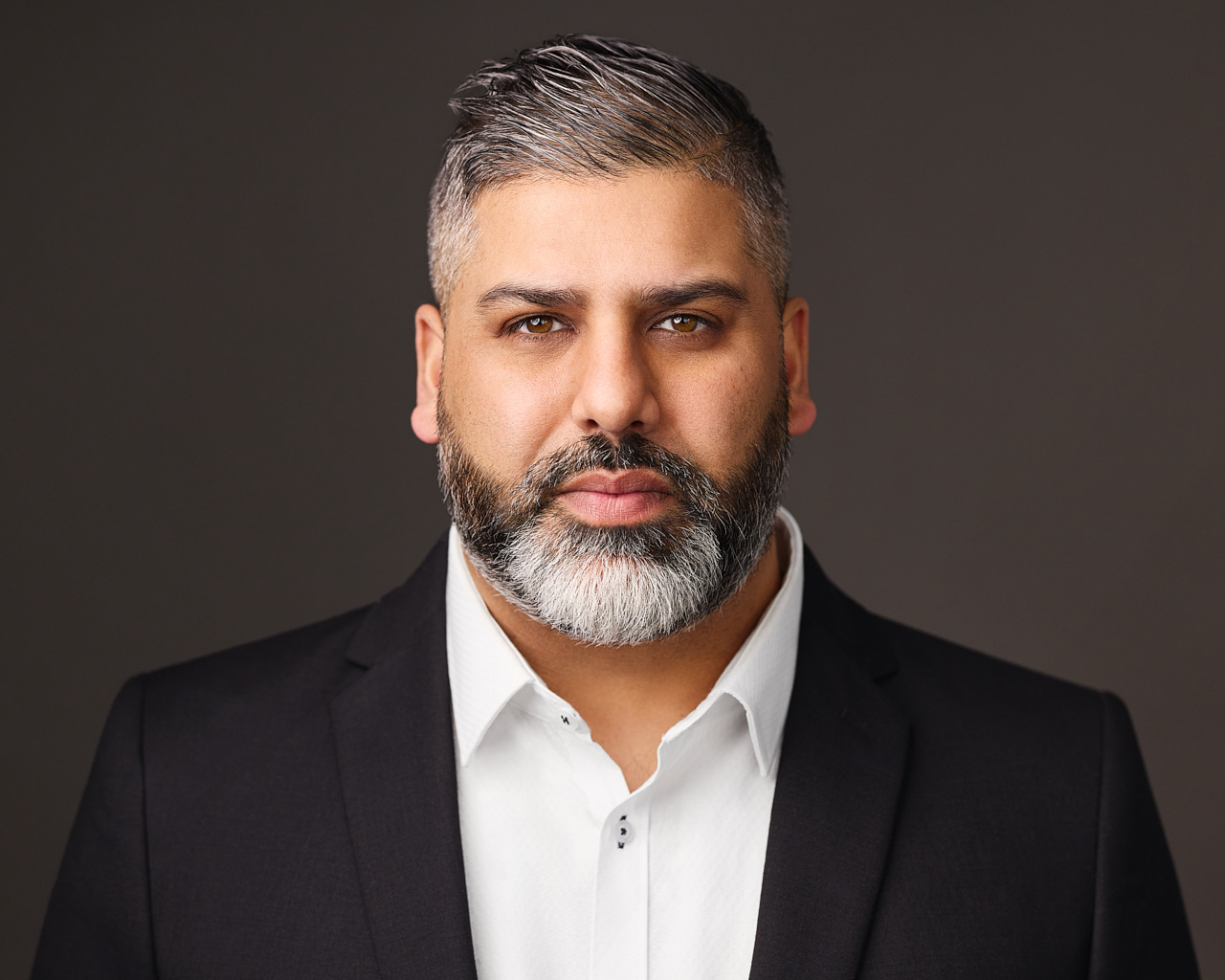 A professional business headshot of a man with a stern expression.