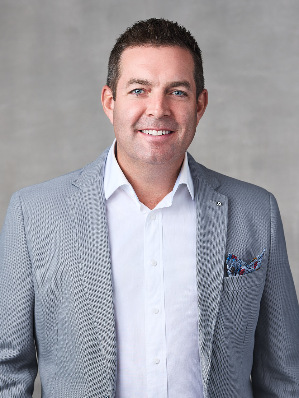 Professional headshot of a Mac's II Agencies team member, dressed in business attire with a poised and confident stance against a clean, white background in Metro Vancouver.