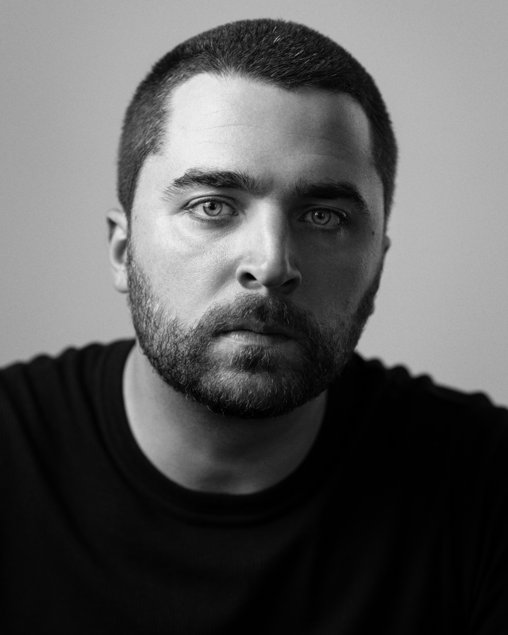 A headshot of an actor with a buzz cut and beard.