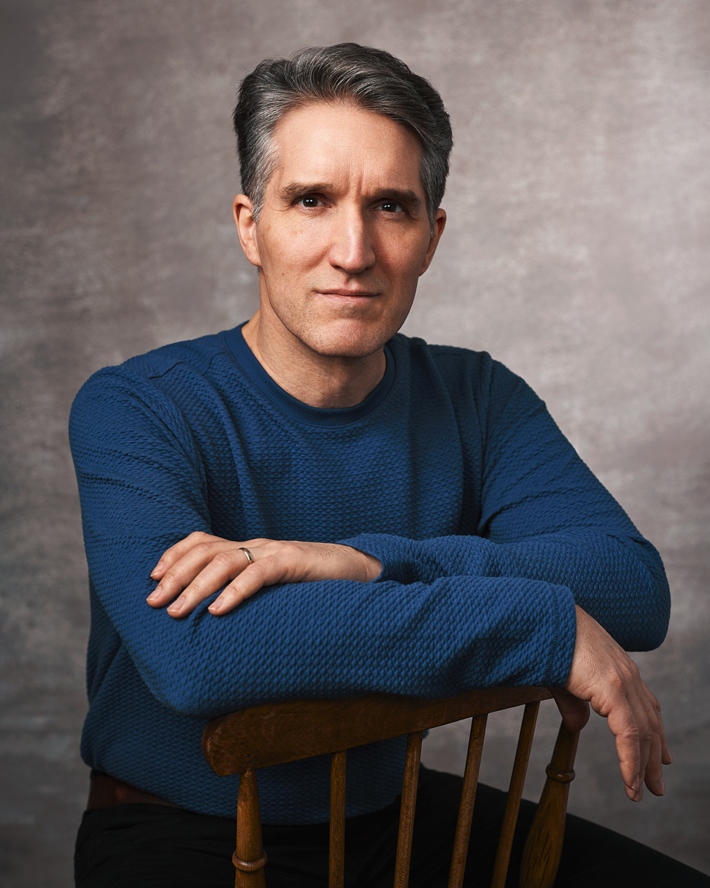 A creative business portrait of a man wearing a blue sweater, sitting on a chair.