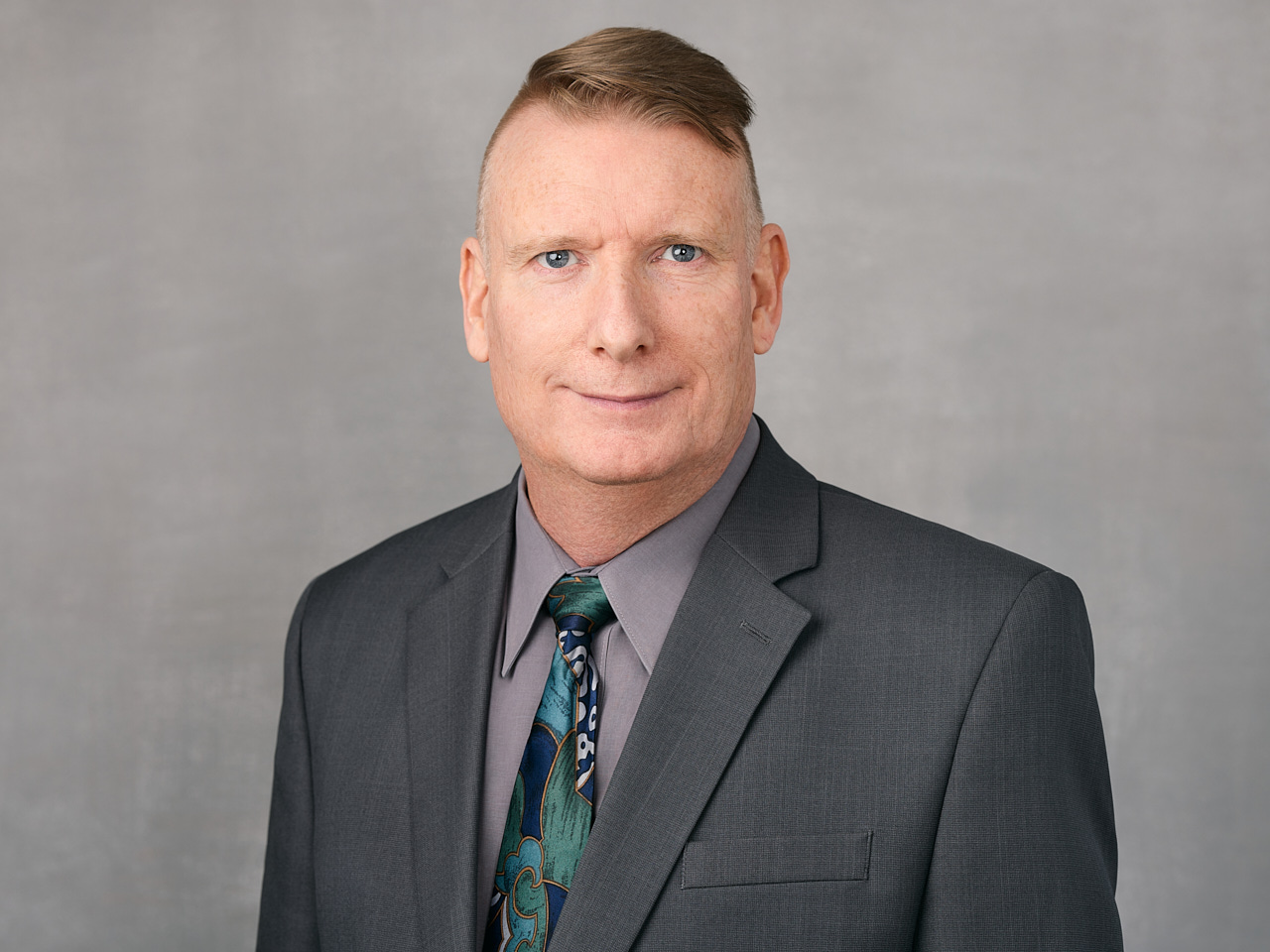 A professional headshot of a Tillicum Agencies team member dressed in business attire with a modern and professional appearance against a light grey background in Maple Ridge.