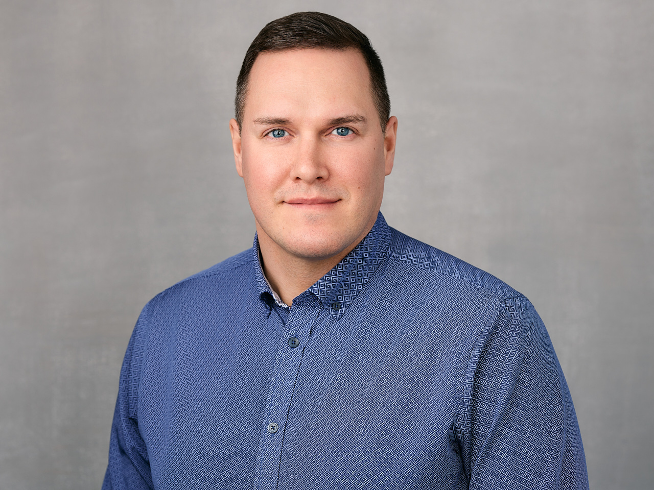 A professional headshot of a Tillicum Agencies team member dressed in business attire with a modern and professional appearance against a light grey background in Maple Ridge.